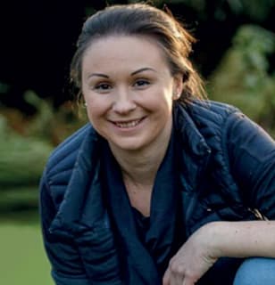 Freundliches Outdoor-Portrait einer Jungen Frau Junge Frau mit dunklen Haaren lächelt freundlich im Freien, trägt blaue Steppjacke